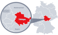Diese Grafik zeigt eine Karte von Deutschland mit einer detaillierten Ansicht der Region Thüringen. Thüringen ist in Rot hervorgehoben und liegt im westlichen Teil Deutschlands. Ein Lupensymbol vergrößert diesen Bereich, um die Lage genauer darzustellen. 